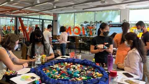A room full of people sitting and standing around tables covered in Lego
