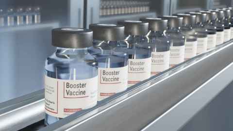 Clear bottles with 'Booster Vaccine' written on them lined up on a conveyor belt.