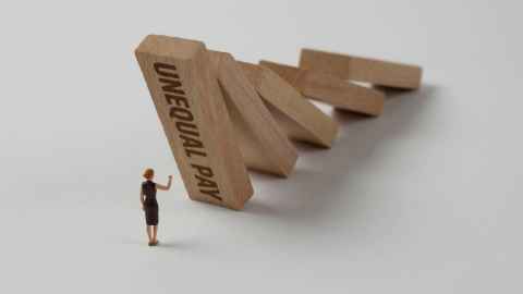 A tiny female figure putting up a hand to stop a massive wooden block with 'Unequal pay' written on it falling on her.