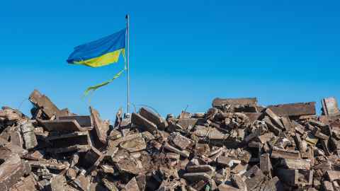 A tattered Ukrainian flag flying over ruins.
