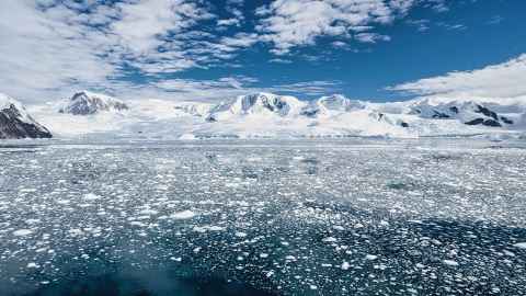 A frozen ocean with hilly, snow-covered land in the background and a blue sky above.