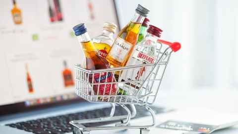 A tiny shopping trolley filled with miniature bottles of spirits, sitting on a laptop.
