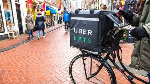 A bicycle with an insulated bag with Uber Eats written on it, parked on a busy pedestrian shopping street.
