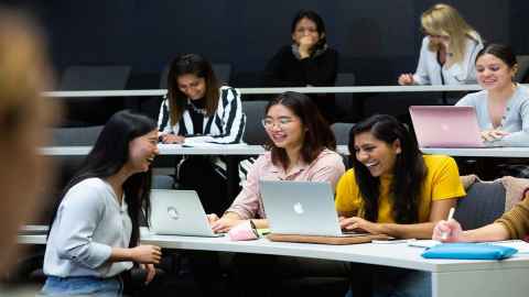 A group of young women sitting in a lecture theatre, talking and laughing.