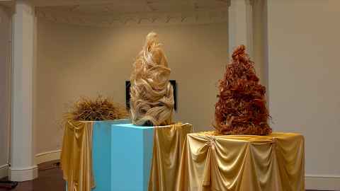 Three wigs of different colours on plinths.