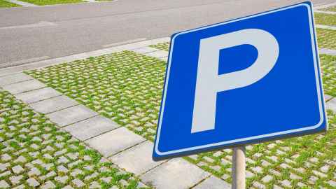 A parking sign over a concrete-tiled driveway.