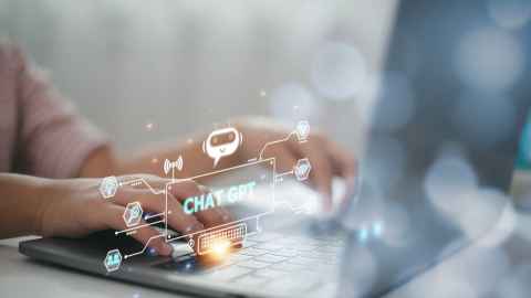 A person typing on a laptop with a stylised image floating in the air with the words 'Chat GPT'.