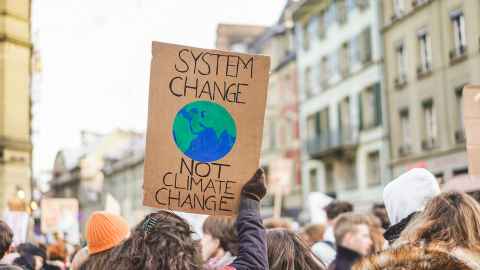 People gathered in protest; a sign in the foreground reads 'System change not climate change'.