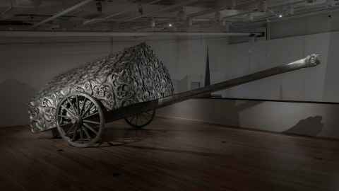 A silver thing on a trailer with wagon wheels.