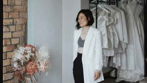 Designer Katie Yeung standing in her studio with a row of wedding dresses behind her