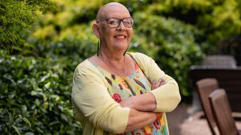 Lisa Finucane is smiling and wearing glasses and bright colours. She has a bald head from chemotherapy. 