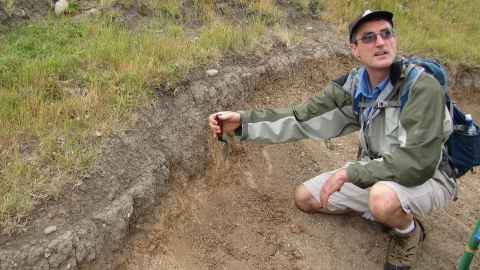 Professor Thegn Ladefoged crouches down by an excavation site on Ahuahu, Great Mercury Island.