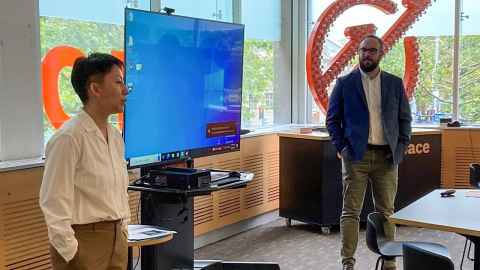 Two people and a blue screen at the front of a room.
