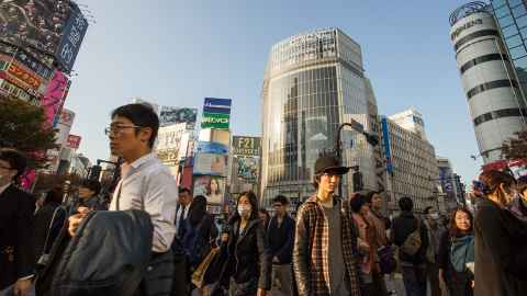 A busy intersection in Tokyo, with dozens of commuters on foot and tall buildings in the background.