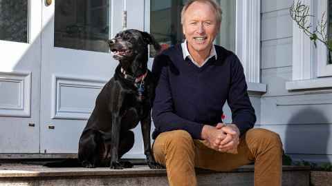 Sam Elworthy sitting on the steps of his home with his black Labrador dog.