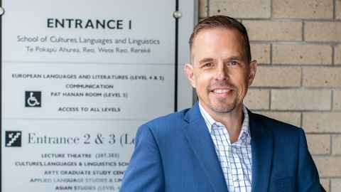 Luke Goode stands besides the School of Culture, Languages and Linguistics