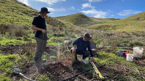 Two people on an archaeological dig among rolling hills.