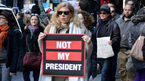 A woman at the front of a protest group with a sign that reads 'Not my president'.