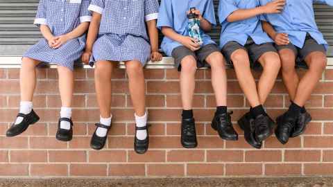 Legs of school kids in uniform, against a brick wall 