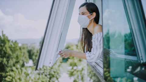 A woman in a surgical mask looking out a window.