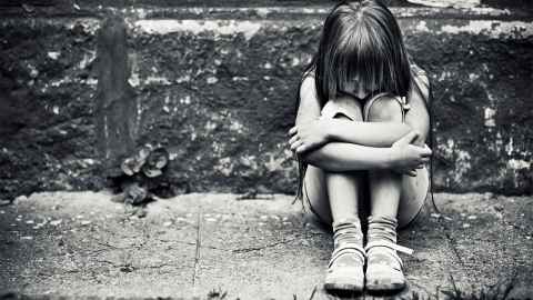 A young girl hugging herself, in black and white.