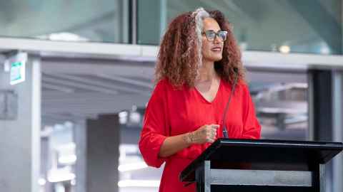 A curly-haired woman standing at a lectern.