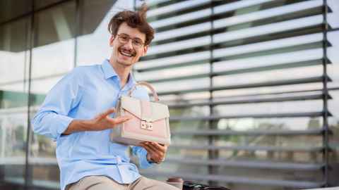 A young man showing off a pink handbag.