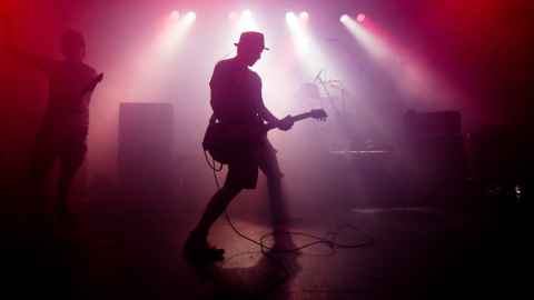 A musician playing electric guitar on a dimly-lit stage.