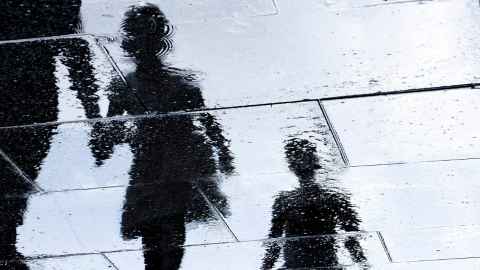 Silhouettes of children reflected on wet concrete.