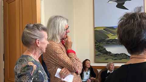 Greg O'Brien and Doris de Pont with Fred Graham and whānau in the background under a Don Binney artwork.