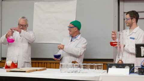 Dr David Ware, Professor David Williams and doctoral candidate Robert Deas at the Incredible Science event in June 2023. There are all holding glass bottles with different colour liquid in each 