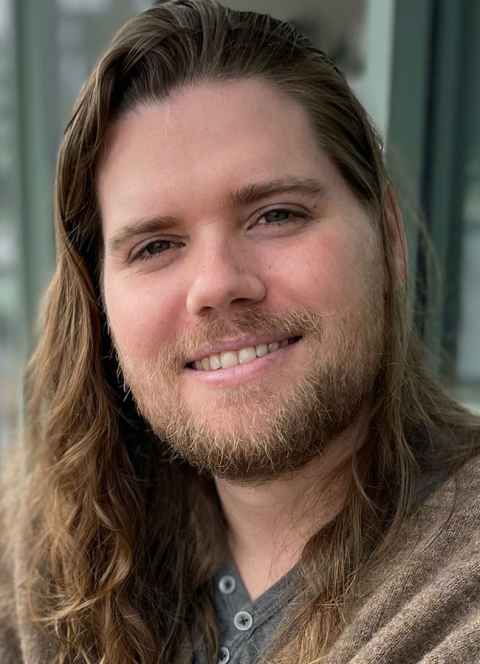 A man with long brown hair and a beard, smiling.
