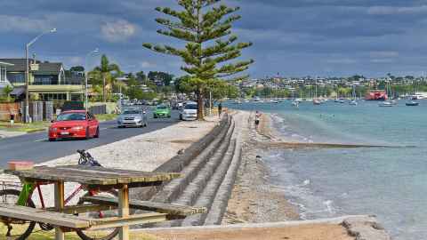 An image of The Parade, Bucklands Beach. The road on the left and sea on the right are divided by a sea wall.