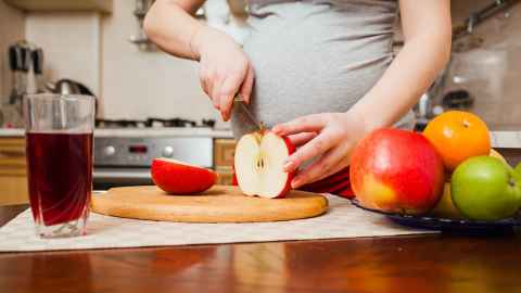 Pregnant woman cutting fruit in her kitchen