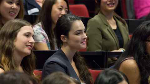 A young woman seated in the middle of a lecture hall