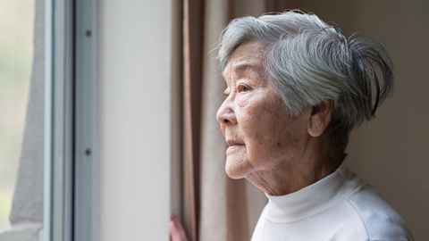 Elderly Chinese woman looks out of a window