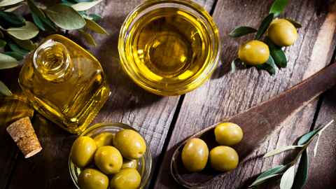 Olive oil in bowl, surrounded by green olives 