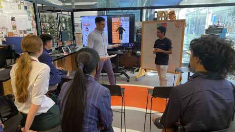 Secondary school students watching two presenters in front of a screen and a whiteboard