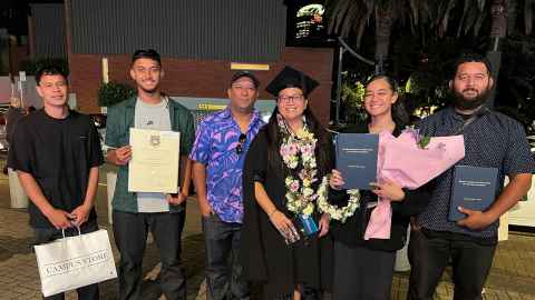 Metua Daniel-Atutolu stands surrounded by her husband and children with her graduation flowers and dissertation