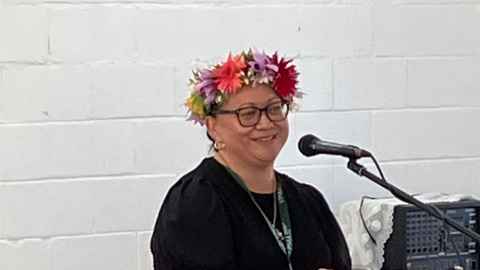 Metua Daniel-Atutolu wearing a ei katu flower garland speaking into a microphone