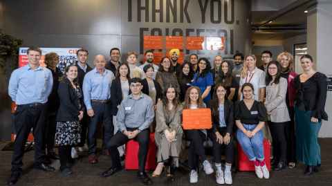 A large group of people in the University's Unleash Space, holding an orange plaque.