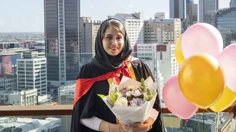 Shima with graduation regalia, balloons and Auckland cityscape behind