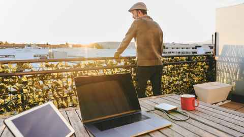 Man on balcony, overlooking sea, with lap top on table in foreground