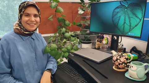 Farha at her desk with her kawakawa plant, teapot and pic of kawakawa on her computer