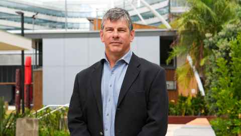 A head and shoulders portrait of Professor Martin Wilkinson wearing a light blue long-sleeved shirt and dark blazer.