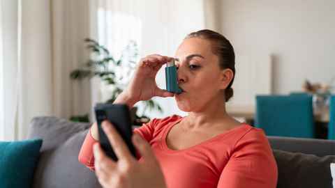 Women using asthma inhaler while looking at phone