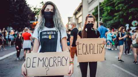 Two women protestors carrying signs, one marked democracy the other marked equality