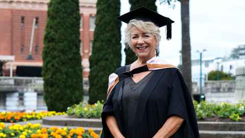 Photo of well-known food writer Julie Biuso in her academic regalia outside the old Railway Station in downtown Auckland.