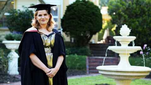 Sophie Scott-Elvidge in her graduation robes with a fountain and Old Government House gardens in the background. Sophie Scott-Elvidge in her graduation robes with a fountain and Old Government House gardens in the background.