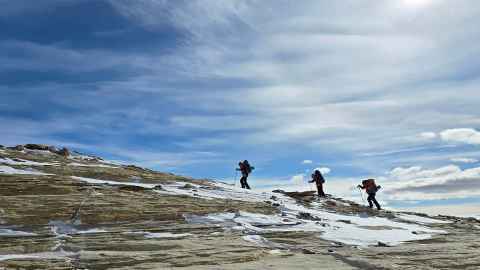 James Muirhead, Sandra Rodrigues and Zoe Armstrong silhouetted against the sky at Upper Wright Valley, climbing along a ridge to explore another outcrop.